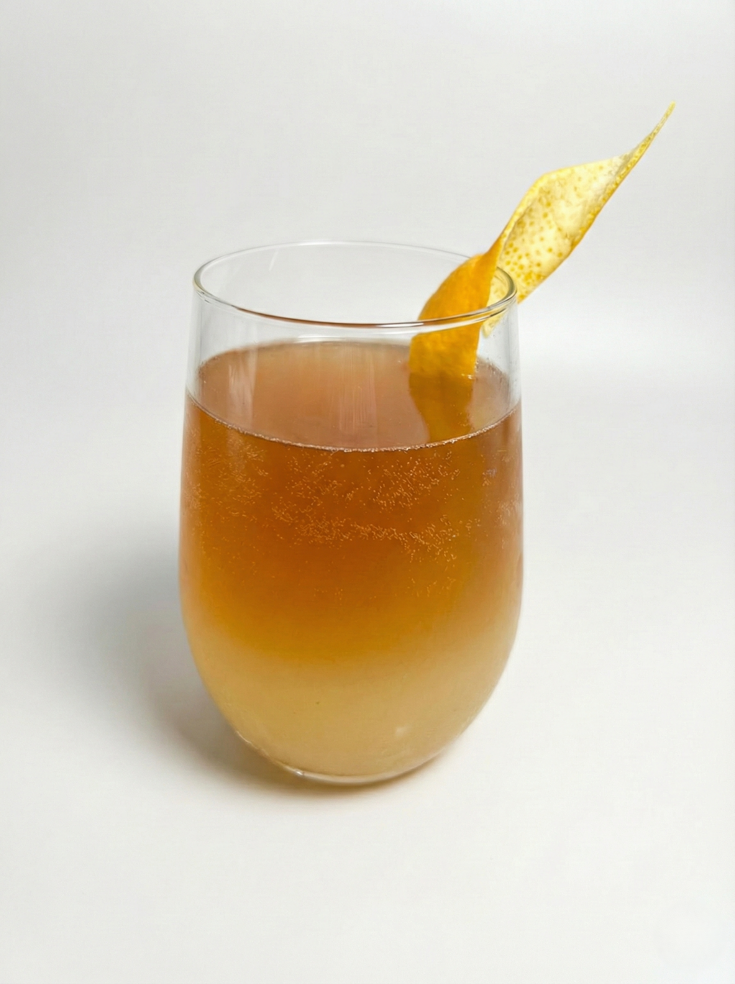 Refreshing Cold Brut Amazai mocktail featuring layered roasted açaí seed coffee and sparkling citrus, served over ice with an orange peel garnish